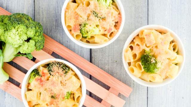 Broccoli macaroni and cheese in three ramekins with a wooden cutting board.