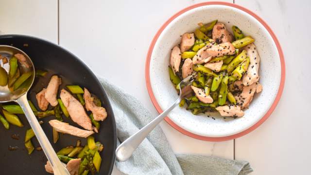 Chicken and asparagus stir fry with thinly sliced chicken breast, chopped asparagus, stir fry sauce, and sesame seeds in a bowl.