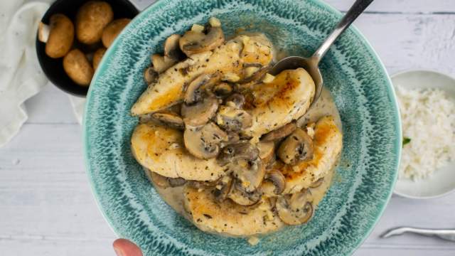 Mushroom chicken with a creamy garlic sauce in a blue bowl.