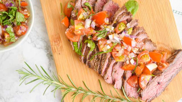 Flank steak with tomato basil salad on a cutting board with rosemary.