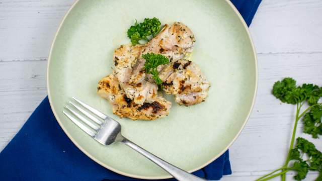 Greek chicken thighs with fresh parsley on a plate with a blue napkin.