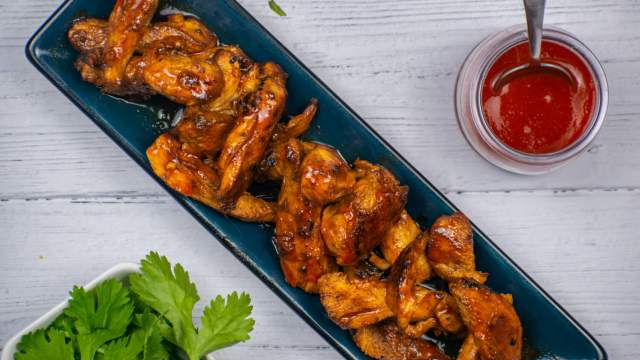 Honey sriracha chicken on a blue plate with Sriracha on the side and lime juice.