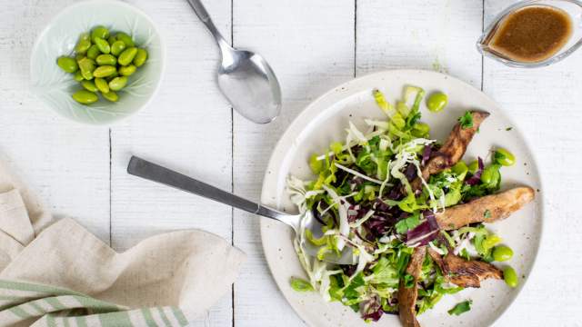 Chinese Chicken Salad with sesame dressing, chicken, edamame, and cabbage on a plate with a fork and spoon.