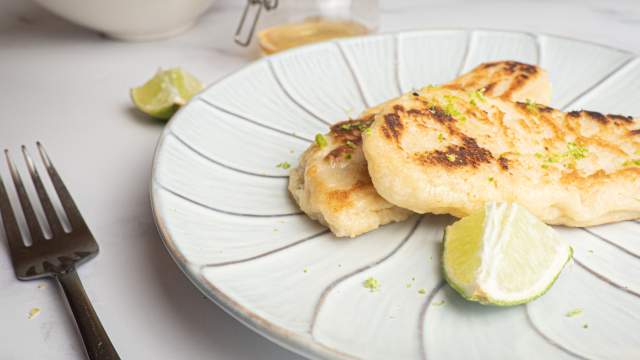 Tilapia with honey and lime cooked until crispy on a plate with a lime and fork.