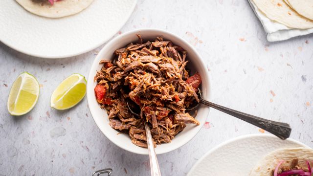 Mexican shredded beef in a bowl with tomatoes and chipotle peppers with tacos on the side.