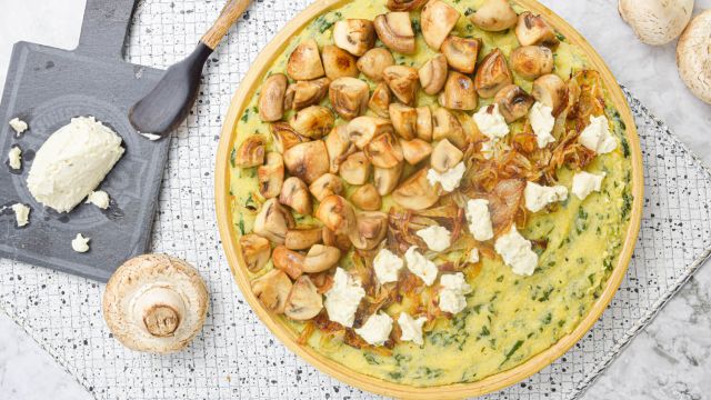 Mushroom spinach polenta with goat cheese on a platter with extra cheese on the side.