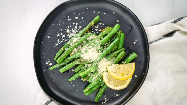 Parmesan green beans with lemon and garlic on a black plate.