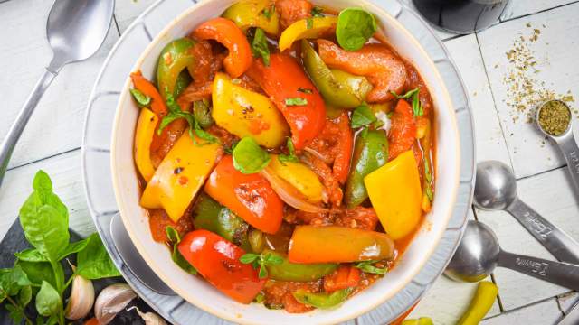 Pepperonata with bell peppers, sweet onion, Roma tomatoes, and garlic in a bowl with fresh basil and spices.