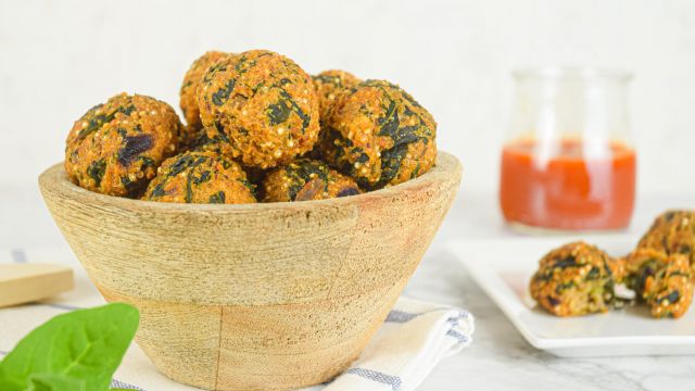 Quinoa meatballs with spinach in a bowl with basil and marinara sauce on the side.