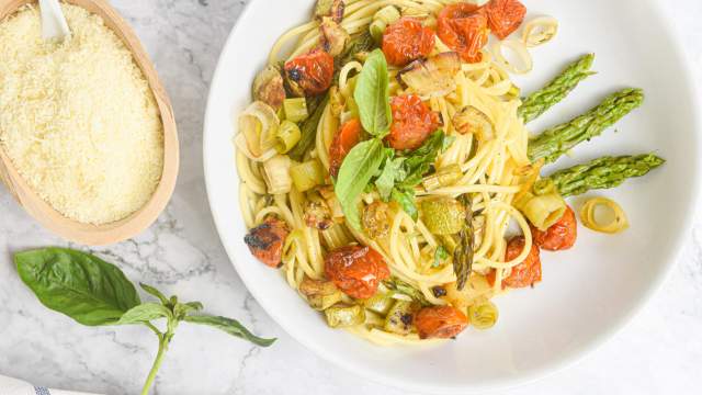 Roasted vegetable pasta with tomatoes, asparagus, onions, and leeks with Parmesan and basil on the side.