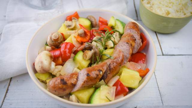 Chicken sausage and vegetable skillet with mushrooms, zucchini, peppers, onions, and rosemary in a bowl.