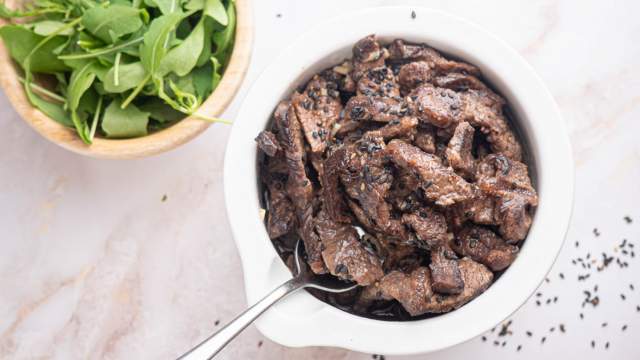 Sesame beef with thinly sliced flank steak in a sesame sauce in a bowl with sesame seeds.