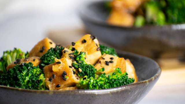 Sesame tofu with broccoli and sesame seeds in a small gray bowl.