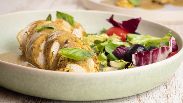 Slow cooker coconut basil chicken on a plate with creamy sauce and salad on the side.