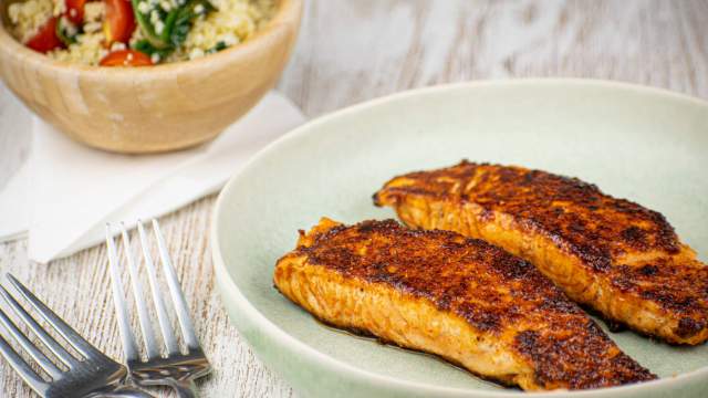 Sweet and spicy salmon with a spice crust on a plate with salad in the background.