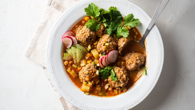 Albondigas soup with Mexican beef meatballs, carrots, zucchini, corn, and onions in tomato broth in a white bowl with cilantro.