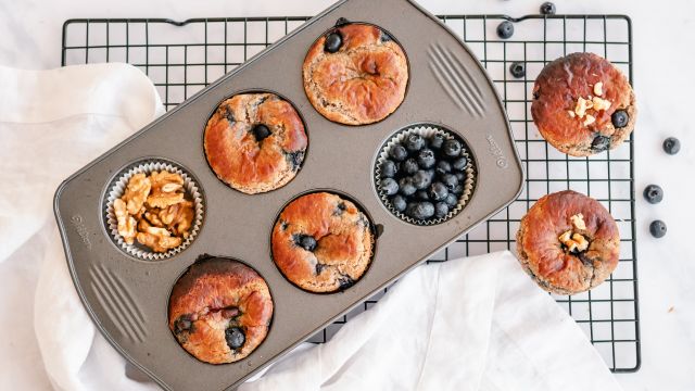 Almond flour yogurt blueberry muffins in a muffin tray with extra blueberries and walnuts on the side.