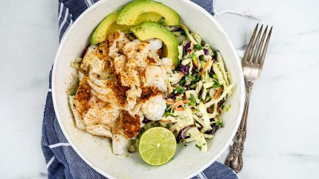 Ancho fish taco bowl with lime slaw and sliced avocado with a blue napkin.