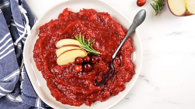 Apple cranberry sauce with fresh cranberries, aplpes, and rosemary in a bowl with a spoon and blue napkin.