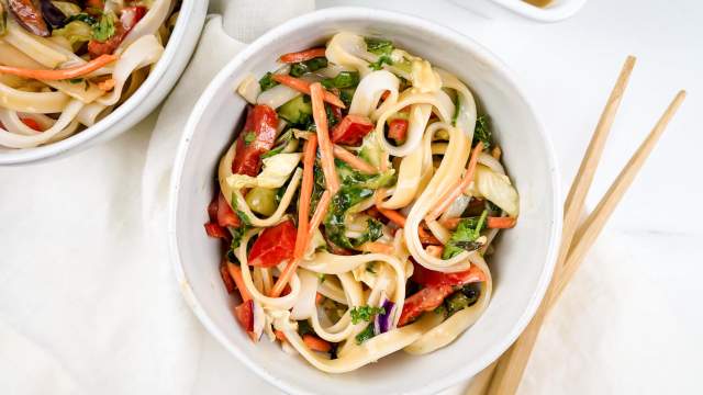 Asian noodle salad with almond dressing, rice noodles, and vegetables in a bowl with chopsticks.