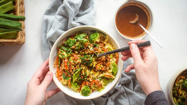 Asian quinoa stir fry with broccoli, carrots, cabbage, and snow peas in a bowl with stir fry sauce and sesame seeds.