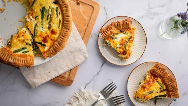 Asparagus quiche with eggs, shredded cheese, asparagus, and red onions cooked in a golden brown crust and served on plates.