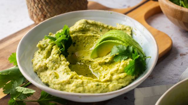 Avocado hummus in a bowl with cilantro and sliced fresh avocado.