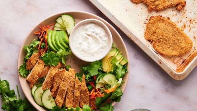 Baked chicken cutlets on a plate with salad and ranch dressing.