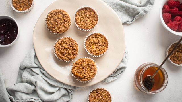 Baked oatmeal muffins with bananas served on a plate with raspberries and maple syrup on the side.