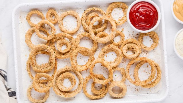 Baked onion rings with a golden brown breadcrumb coating on a baking sheet with ketchup on the side.