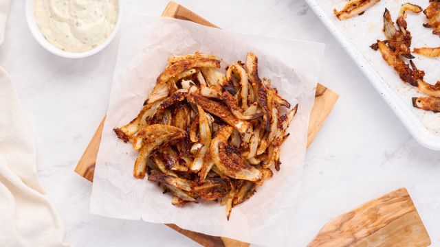 Baked onion straws with a crispy Parmesan coating on parchment paper with dipping sauce on the side. 