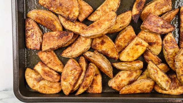 Crispy baked potato wedges on a cooking sheet with paprika, garlic powder, salt, and pepper.