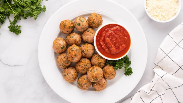 Baked turkey meatballs with parsley and Parmesan cheese on a plate with marinara sauce.