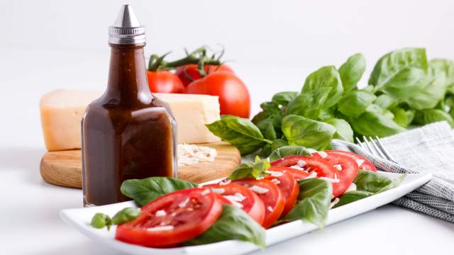 Balsamic vinaigrette in a glass jar with a tomato and basil salad.