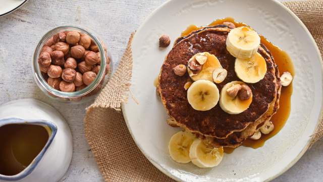 Banana oat pancakes made with mashed bananas and rolled oats stacked on a plate with maple syrup. 