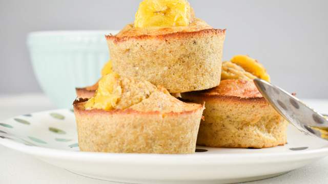 Banana muffins with quinoa and chia seeds with a sliced banana on top stacked on a plate.