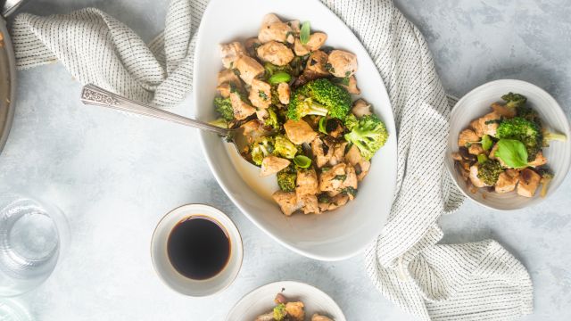 Basil chicken stir fry with broccoli florets, fresh lemon, soy sauce, and red pepper flakes in a bowl with a spoon.