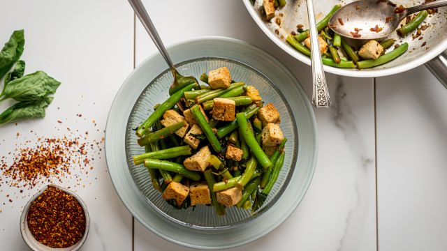 Basil tofu with green beans in a glass bowl with a skillet on the side.