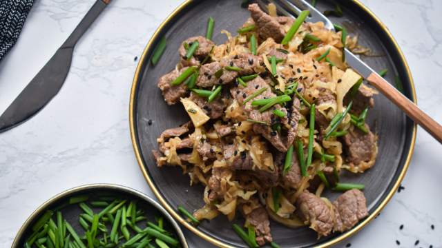 Beef and cabbage stir fry with garlic, green onions, and sesame seeds on a plate with chopsticks.