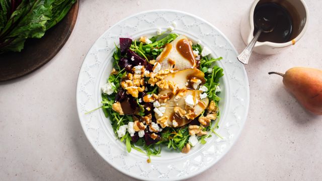 Beet salad with goat cheese, pears, walnuts, arugula, and a blasamic dressing in a white bowll.