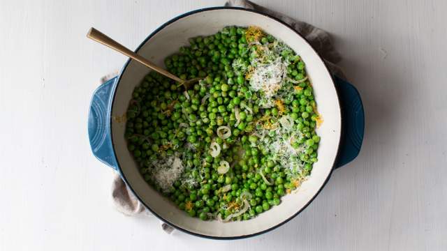 Sauteed peas with garlic, shallots, lemon, and shredded Parmesan cheese in a ceramic dish.