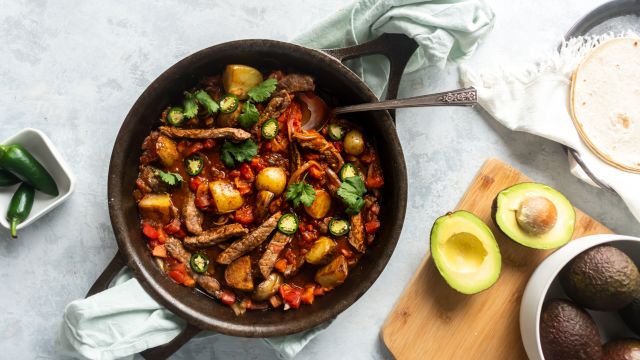 Bistec ranchero with pieces of steak cooked in a tomato and pepper sauce in a skillet.