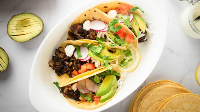 Black bean tacos with chipotle peppers served in corn tortillas topped with avocado, radish, tomatoes, and fresh cilantro.