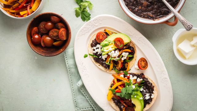 Black bean tostadas served on crispy baked tostada shells with peppers, onions, avocado, cheese, and tomatoes.