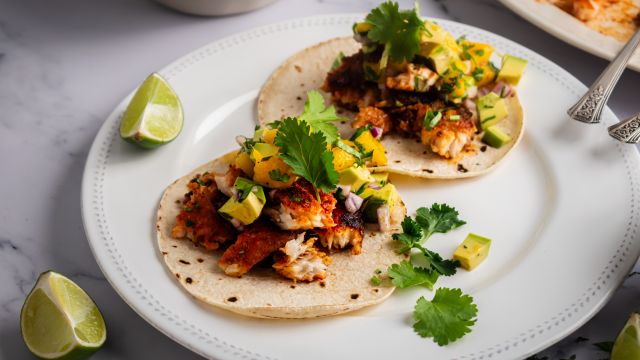 Blackened fish tacos with mango avocado salsa on corn tortillas with fresh cilantro and lime wedges.