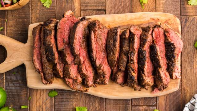 Blackened steak with a charred outside sliced on a wooden cutting board.