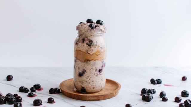 Blueberry overnight oatmeal with almond butter in a mason jar with blueberries on the side.