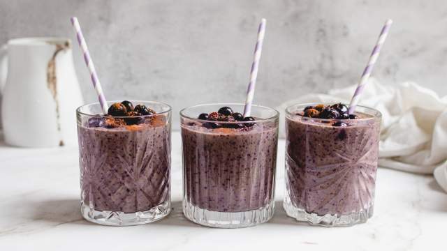 Blueberry banana smoothie with frozen bananas, blueberries, and spinach blended in a glass with blueberries on top. 