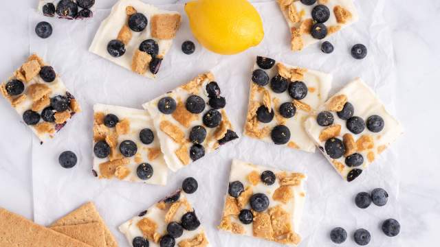 Blueberry lemon frozen yogurt bark with graham crackers on a white board with fresh lemon and blueberries.