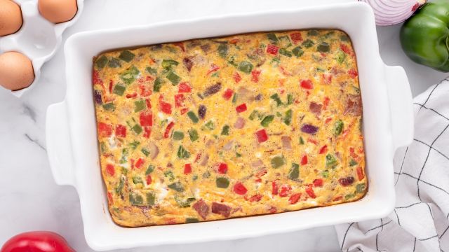 Breakfast egg casserole with turkey bacon, cheddar cheese, peppers, and onions in a baking dish.